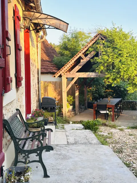 Het terras langs het huis met een bankje, de barbecue en de pergola