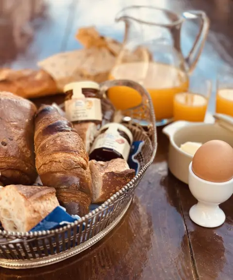 Ontbijt op tafel: stokbrood, croissants, een gekookt eitje, potjes jam en verse jus