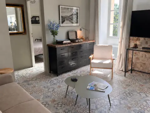 De woonkamer met een ladenkast, leesstoel en salontafel op de oude cementtegels, met doorkijk naar de slaapkamer